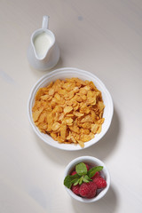 Breakfast set: сornflakes, milk and raspberry with mint leaves on a light wooden background. Top view