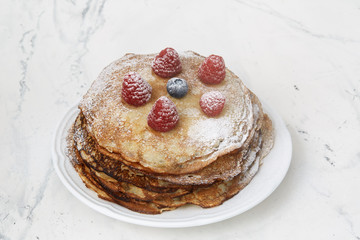 Homemade pancakes decorated with raspberries and blueberries, sprinkled with powdered sugar, on a light background