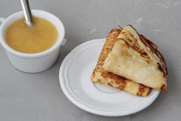 Homemade pancakes served with honey, crepes on a plate on a grey concrete background