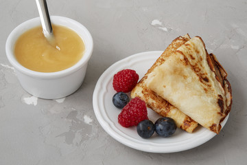 Homemade pancakes or crepes served with honey, raspberries and blueberries