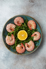 Shrimp salad with shrimps, arugula, lemon on blue plate. Top view