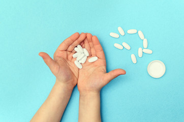 Fototapeta na wymiar A small child holds in his hand a handful of pills that lie on a blue background. White pills in child hands.