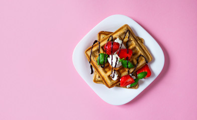Belgium waffles dessert with strawberries, ricotta cheese and chocolate on pink background.