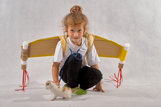 A little girl with cardboard wings playing with a kitten in the doctor