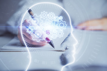 Double exposure of woman's writing hand on background with brain hologram. Concept of brainstorming.