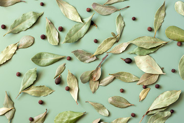 Bay leaves (Laurus nobilis) and black pepper scattered on green background