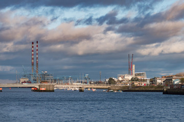 Fototapeta na wymiar Wide view over docks area in Dublin, Ireland with many boats, cranes and Poolsbeg Power Station chimneys
