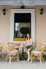 Romantic young girl with beautiful makeup sits at a table of a street cafe. Next to her on the table is a bouquet of roses. The concept of waiting for happiness, a date.