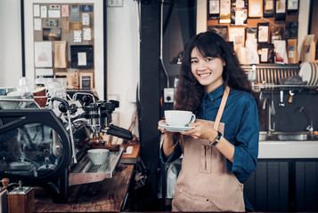 Asian Barista served coffee up with smile at cafe holding mug with two hand with smiling face at cafe bar background.