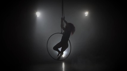 Silhouette young caucasian brunette sportive dancer female balancer in beige leotard back lying hang on aerial hoop on three rays of light background 029