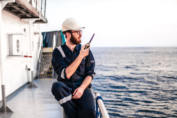 Obraz premium Deck Officer on deck of offshore vessel or ship , wearing PPE personal protective equipment. He holds VHF walkie-talkie radio in hands. Dream work at sea