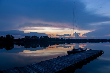 Zachód słońca nad jeziorem Kalwa w Polsce. Odbicie nieba w wodzie, łódź żaglowa przy...