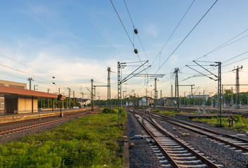 Outdoor view of straight and curve railway track lines without train at train station with mess complex electric cables and poles with golden light atmosphere against evening before sunset sky.