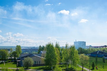 Fototapeta premium Summer industrial landscape - the roofs of industrial buildings against the blue sky with white clouds, in the background - thermal power plants and overhead crane