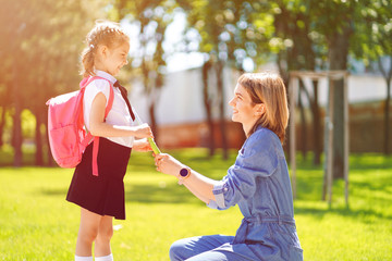 First day at school. Mother leads a little child school girl in first grade. Woman and girl with backpack behind the back. Beginning of lessons. First day of fall