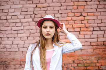 close up portrait of beautiful stylish kid girl in hat near pink brick wall as background