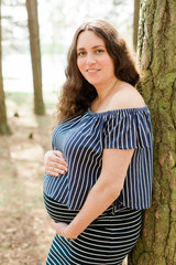 Fototapeta premium Cheerful pregnant woman with long hair standing in the forest