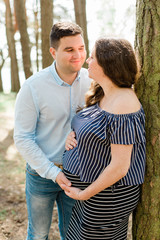 Cheerful pregnant woman with long hair standing on the beach with her husband behind. Young family expecting a child. Happy pregnancy concept.