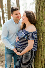 Naklejka premium Cheerful pregnant woman with long hair standing on the beach with her husband behind. Young family expecting a child. Happy pregnancy concept.