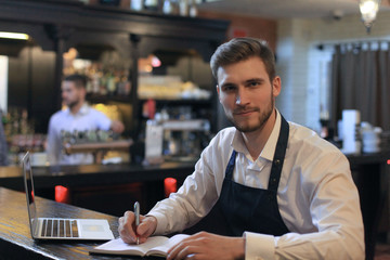 Happy cafe manager counting recipes with laptop.