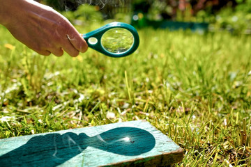 Man holding a magnifying glass making fire, focused on wood on summer day.