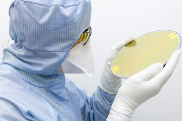 An engineer working in a clear room wearing a special uniform and protective glasses holds silicon...