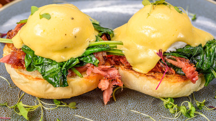 A serving of two Eggs Benedict, with a muffin base, ham, poached eggs and hollandaise sauce
