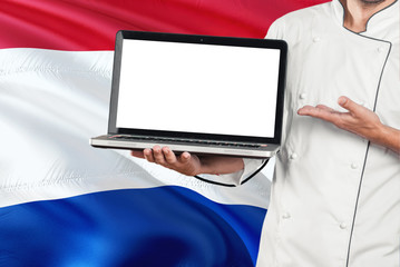 Paraguayan Chef holding laptop with blank screen on Paraguay flag background. Cook wearing uniform and pointing laptop for copy space.