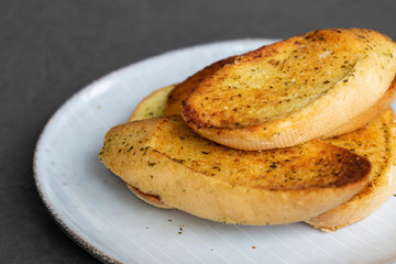 Garlic bread toasted and sliced on a plate,  with a grey tile background