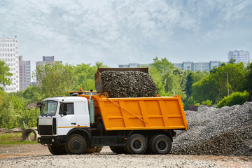 Obraz premium Large front loader loading dumper truck, tipper next to pile of gravel over blue sky. Heavy duty truck loading with rubble and stones. Wheel loader loads a truck with gravel on costruction site.