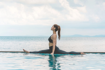 Asian young woman practice Yoga Monkey God Pose or Yoga Hanumanasana pose on the pool above the beach in the morning with beautiful sea in Tropical island,Feeling comfortable and relax in holiday