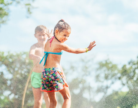 Two children play with sprinkling water in summer garden
