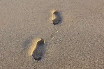 two human footprints in the fine sand at sunset