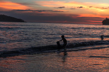 Junge streichelt Hund beim Sonnenuntergang am Strand