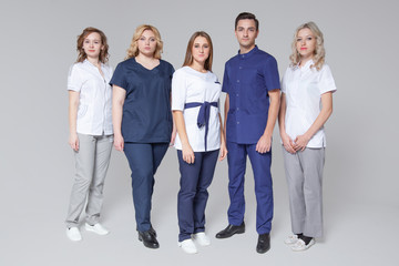 Successful team of medical doctors are looking at camera while standing on grey background