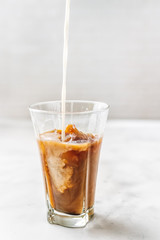 Iced coffee with pouring milk in glass on white background