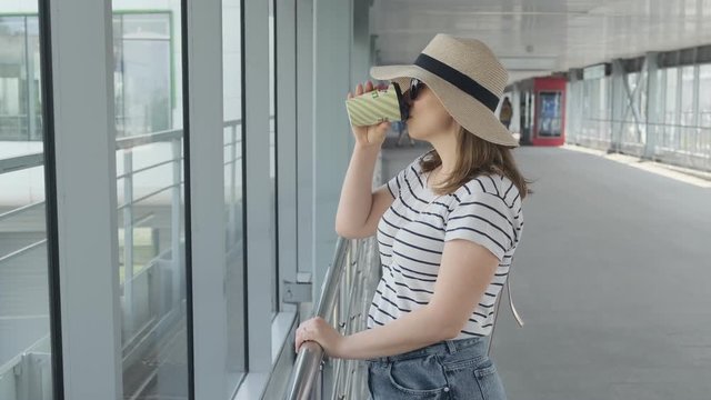 Woman drinking cup of coffee while waiting plane in airport. Medium shot with copy space