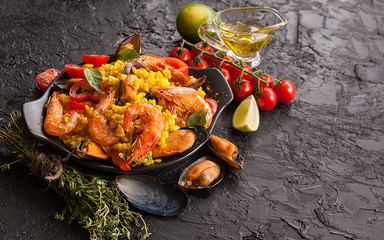 Paella on a pan with shrimp, mussels on a black table. Spanish Mediterranean cuisine. Seafood is a...