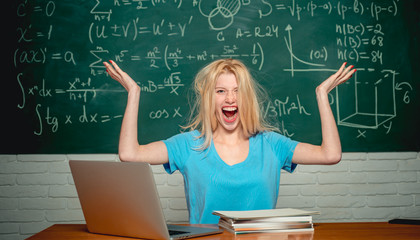 Bored student doing homework on line with a laptop. Student tired of studying in classroom. High school. Negative facial expression. Unhappy student working on laptop. Learning.