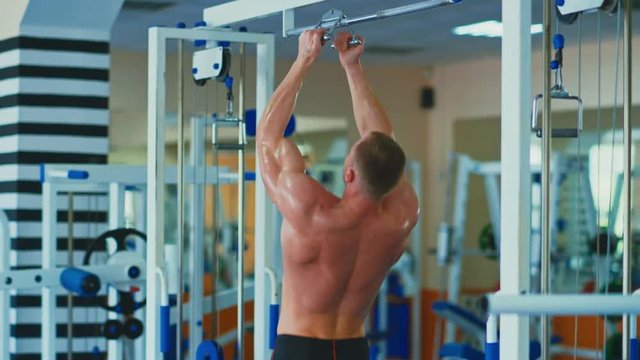 Training in the gym. Shirtless muscular man doing pull-ups on bars at fitness club
