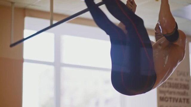 Shirtless muscular man doing pull-ups on bars at gym