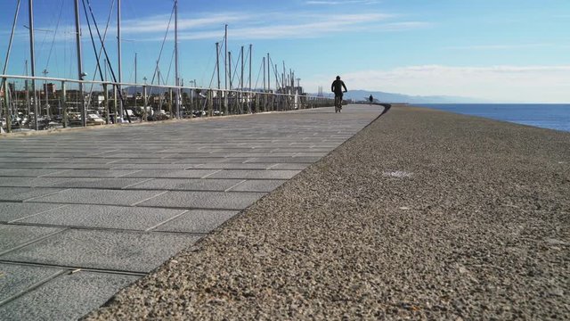 People run on the waterfront. Sunny summer day. Jogging in the fresh sea air. People ride bicycles and take pictures of the sea. Azure birch. Rocky promenade by the sea. Man runs on the street