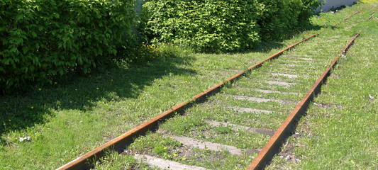 A rut of rusty rails and wooden sleepers in green grass