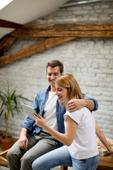 Couple is using a digital tablet and smiling while sitting on the table at home