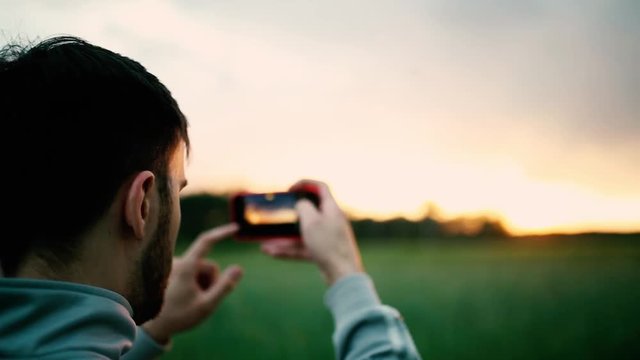 young man photographing sunset in nature with a smartphone camera