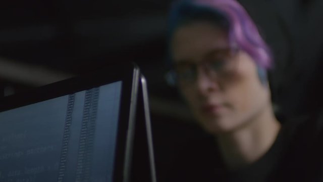 Rack focused shot of processing program code on computer screen and female hipster sitting nearby and looking at computer screen