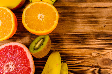 Still life with exotic fruits. Bananas, mango, oranges, grapefruit and kiwi fruits on wooden table. Top view