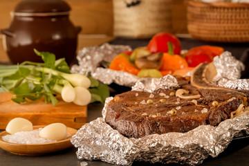 Meat steak baked in foil and baked vegetables on a wooden table with fresh tomatoes and greens. Close-up