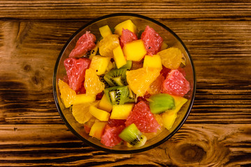 Salad with mango, oranges, grapefruit and kiwi fruits in a glass bowl on wooden table. Top view
