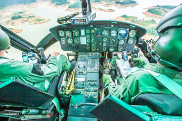 Military helicopter cockpit with two pilots flying over a tropical lake.